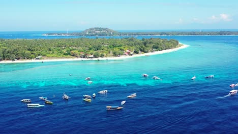 Tropical-Paradise-Island-Of-White-Sand-Filled-With-Green-Trees-Surrounded-By-Bright-Blue-Sea-Waters-With-Boats-Adrift,-Indonesia---Aerial-Drone-Shot