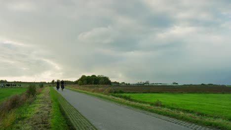 Two-people-riding-their-bicycle-on-a-rural-road-near-Middelburg,-the-Netherlands