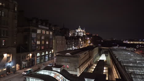 Panning-shot-of-Edinburgh-at-night-from-North-Bridge-with-Edinburgh-Royal-hotel,-Waverley-railway-station,-castle-and-Scott-monument