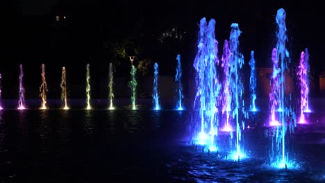 Fountain-illuminated-at-night-in-city-park,-abstract-lights-with-changing-colors-from-multiply-nozzles-in-circle