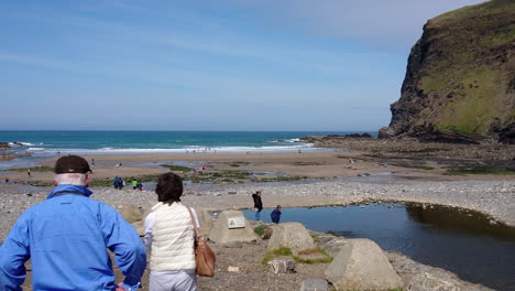 A-couple-of-senior-tourists-stop-at-Crackington-Haven-beach-in-Cornwall,-United-Kingdom,-where-walkers-swimmers-and-bathers-are-having-fun
