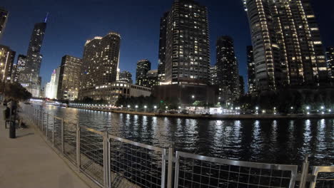 Timelapse-Night-Chicago-riverwalk-view,-Usa,-United-States,-by-the-river,-boats-passing-fast,-downtown,-Skyscrapers,-buildings,-cityscape-and-architecture