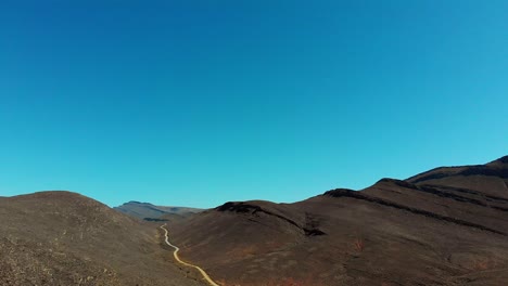 4k-aerial-drone-shot-displaying-mountains-and-mountain-pass-dirt-road-with-clear-blue-sky