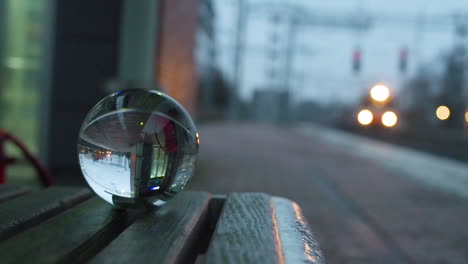 Crystal-ball-on-a-bench-reflects-a-passing-train-at-station
