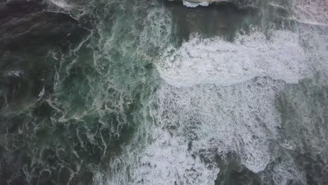 Churning-white-breaking-waves-move-slowly-shoreward,-vertical-aerial
