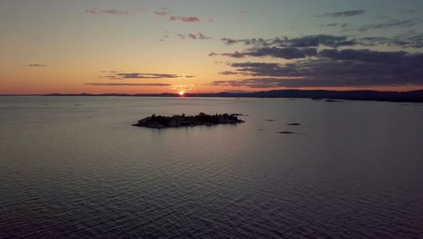 High-View-of-Rocky-Pine-Tree-Island-in-Blue-Lake-at-Sunset,-Drone-Aerial-Wide-Dolly-Out