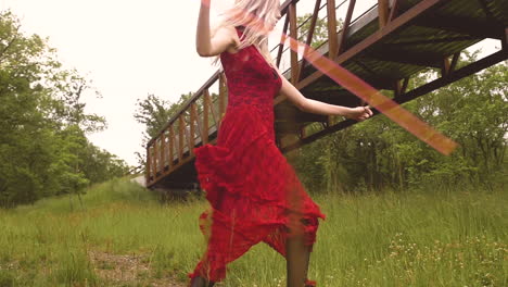 Young-Blonde-Woman-in-a-Red-Dress-dances-around-a-meadow-with-twirling-a-ribbon-wand