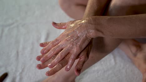 Closeup-of-mature-woman-rubbing-coconut-oil-on-her-hands-preparing-for-leg-massage