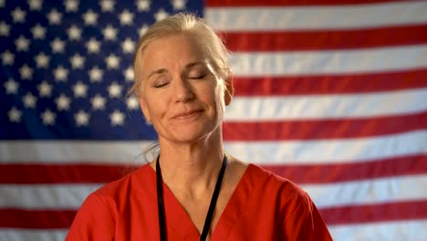 Retrato-Medio-Apretado-De-Una-Enfermera-Que-Parece-Aliviada,-Feliz-Y-Asintiendo-Con-La-Cabeza-Con-La-Bandera-Estadounidense-Detrás-De-Ella