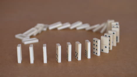 Female-hand-toppling-line-of-white-dominoes-on-table