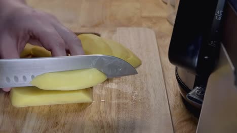 Slow-Motion-Slider-Shot-of-Cutting-a-Potato-into-Fries-on-a-Wooden-Chopping-Board-in-the-Kitchen