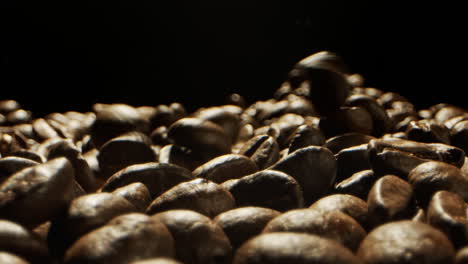Close-Camera-movement-through-falling-fresh-coffee-beans-into-a-pile-of-beans-laying-on-a-wooden-surface