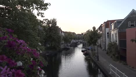 Canal-with-boats-in-the-Netherlands,-after-sunset,-flanked-by-flowers