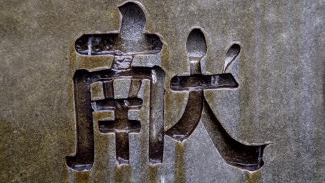 Water-flowing-over-Japanese-kanji-symbol-etched-in-stone,-close-up