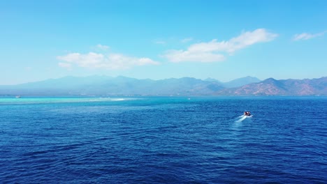 Touring-boat-sailing-across-deep-blue-sea-toward-volcanic-mountain-islands-with-beautiful-coastline-on-a-sunny-summer-day,-Indonesia