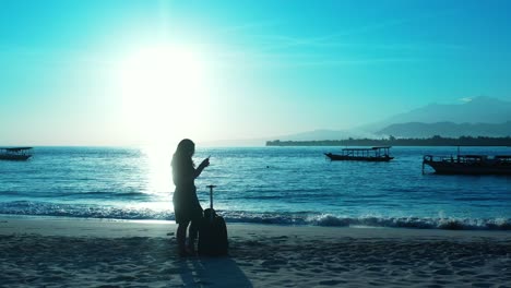 Silhouette-Einer-Touristenfrau-Mit-Reisetasche,-Die-Am-Exotischen-Strand-Bei-Wunderschönem-Sonnenuntergang-Steht-Und-Der-Leuchtende-Himmel-Sich-In-Der-Ruhigen-Lagune-Spiegelt