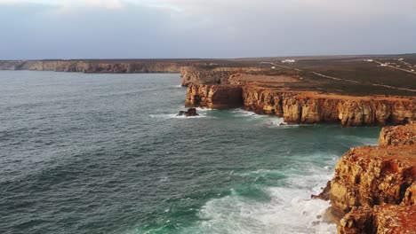 Eroded-red-sea-cliffs-of-Tonel-beach-in-south-Portugal-splashed-by-waves,-Aerial-flyover-reveal-shot