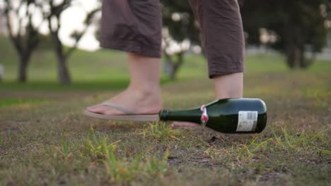 Dramatic-slow-motion-shot-of-a-socially-irresponsible-person-tossing-an-empty-wine-bottle-on-the-ground-whilst-walking-in-a-public-park