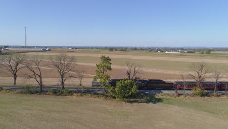 Aerial-of-a-restored-steam-locomotive-moving-slow-and-followed-parallel-to-train-while-pulling-in-on-train-blowing-smoke-and-steam-going-thru-farm-countryside