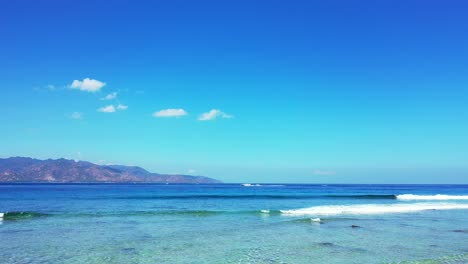 Lebhafte-Farben-Einer-Friedlichen-Meereslandschaft-Mit-Weißen-Wellen,-Die-An-Der-Küste-Einer-Tropischen-Insel-Schäumen,-Blauem-Meer-Und-Hellem-Himmelshintergrund-In-Indonesien