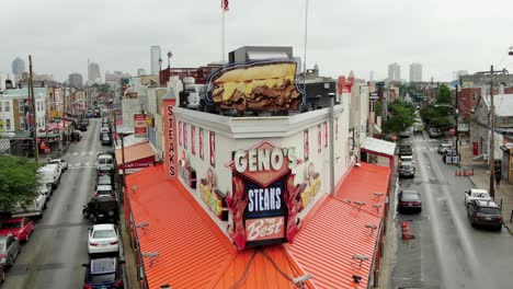 Geno's-Steaks,-famous-Philly-Cheesesteak-with-Philadelphia-skyline-in-distance-during-summer,-American-flag-at-iconic-tourist-stop