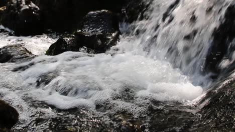 Beschleunigtes-Wasser,-Das-Am-Fuße-Eines-Kleinen-Wasserfalls-Ergießt,-Der-Auf-Allen-Seiten-Von-Felsen-Umgeben-Ist