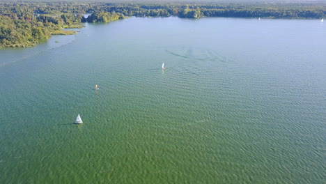 Drone-Volando-Sobre-Un-Lago-Con-Veleros-Y-Windsurfistas-Proyectando-Grandes-Sombras