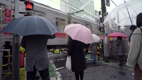 Zug-Fährt-An-Einem-Bahnübergang-Vorbei,-Während-Menschen-Darauf-Warten,-In-Tokio,-Japan,-Zu-überqueren-–-Totale