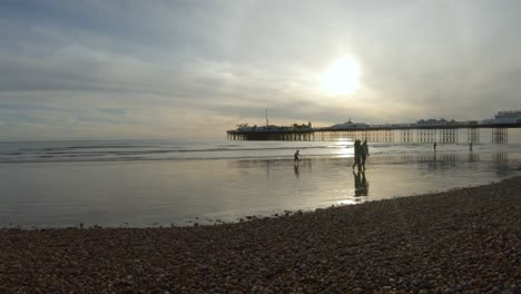 Goldener-Sonnenuntergang-über-Dem-Strand-Von-Brighton-Im-Vereinigten-Königreich-Mit-Menschen,-Die-Spazieren-Gehen-Und-Das-Wasser-Genießen