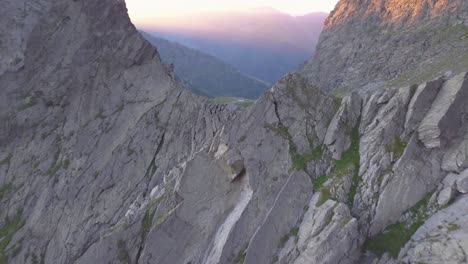 Drohnenansicht,-Die-Auf-Die-Zerklüftete-Bergkette-Hoch-In-Den-Bergen-Rumäniens-Zufliegt,-Mit-Buntem-Licht-Des-Sonnenuntergangs-Auf-Entfernten-Gipfeln-Und-Dem-See,-Der-Unten-Sichtbar-Wird