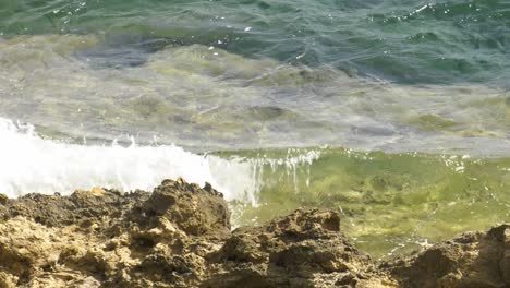 Waves-of-clear-water-washing-onto-jagged-rocks,-mediterranean-sea
