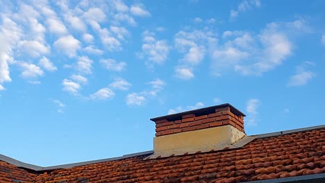 Gemauerter-Schornstein-Auf-Dem-Hausdach-Und-Spärliche-Wolken-Am-Blauen-Himmel,-Die-Rauch-Simulieren
