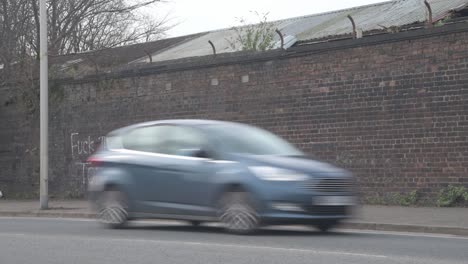 Wide-shot-of-cars-driving-past-an-anti--government-graffiti-on-a-brick-wall