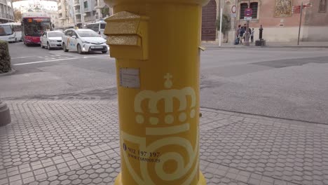 Tilt-Up-of-yellow-Correos-mailbox-in-Seville,-Spain-with-church-in-background