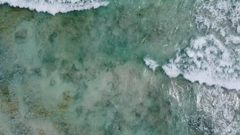 Aerial-top-down-view-of-waves-crashing-over-a-rocky-bottom-of-a-crystal-clear-Caribbean-sea-next-to-Cozumel-Island-in-Mexico