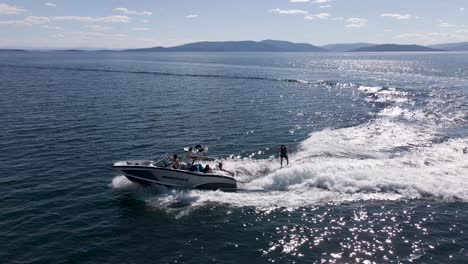Wakesurfer-Folgt-Einem-Motorboot,-Das-An-Einem-Sommertag-über-Das-Dunkelblaue-Wasser-Im-Flathead-Lake,-Kalispell,-Montana-Rast-–-Luftaufnahme