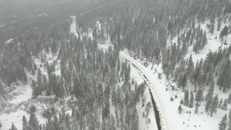 Aerial-tilt-shot-revealing-a-dangerous-mountain-road-covered-by-snow-on-a-foggy-day