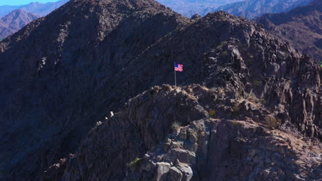 Luftaufnahme-Der-Amerikanischen-Flagge-Auf-Dem-Gipfel-Eines-Berges-Mit-Berghintergrund
