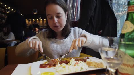 Young-woman-in-restaurant-cutting-large-portion-of-German-wurst-sausage-in-slices