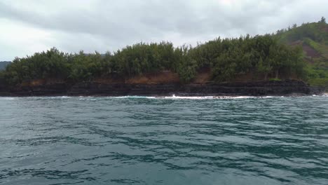 4K-Hawaii-Kauai-Bootfahren-Auf-Dem-Meer,-Das-Von-Rechts-Nach-Links-Schwebt,-Von-Wellen,-Die-An-Der-Felsigen-Küste-Krachen,-Bis-Hin-Zu-Bergen-In-Wolken-In-Der-Ferne