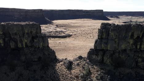 Passing-through-a-towering-butte-to-reveal-the-pristine-canyon-beyond,-Dry-Falls-State-Park,-aerial
