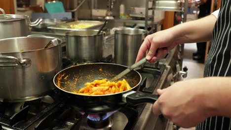Chef-Cooking-And-Stirring-Penne-Pasta-In-A-Skillet-Pan-On-A-Stove-In-The-Kitchen-Of-A-Restaurant