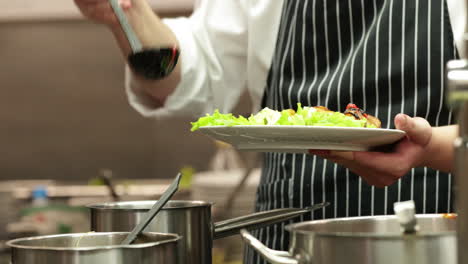 Chef-Pouring-Sauce-On-Top-Of-Salad-On-A-Plate-In-The-Kitchen-Of-A-Restaurant
