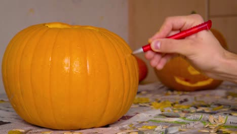 Pumpkin-Carvin-Male-Drawing-Creepy-Face-of-Jack-O'Lantern-onto-Pumpkin-with-Pen-getting-ready-to-carve-Halloween-decoration