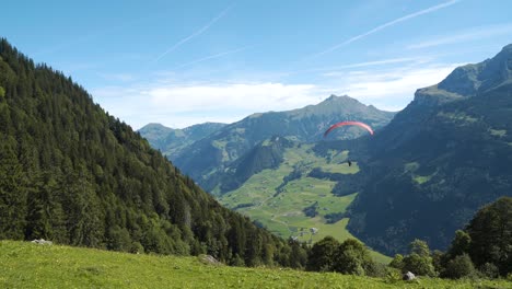 Paraglider-flying-down-the-mountain-in-the-Swiss-Alps,-wide-shot,-handheld