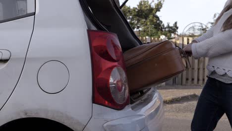 Woman-taking-old-brown-suitcase-out-of-car-boot-wide-shot