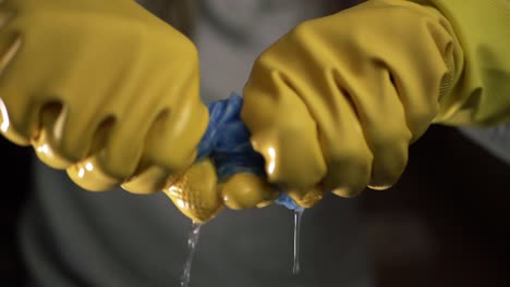 Hands-wringing-out-cleaning-cloth-wearing-yellow-rubber-gloves-medium-shot