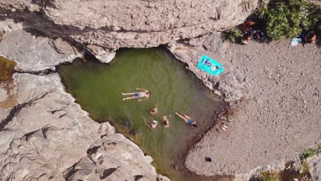 Group-of-friends-enjoy-a-day-of-swimming-at-a-natural-freshwater-pool-in-the-middle-of-a-dry-arid-wadi-valley