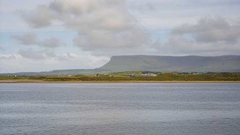 Zeitraffer-Der-Meeresküste-Irlands-Mit-Hügeln-In-Der-Ferne-Und-Sich-Bewegenden-Wolken-Am-Himmel