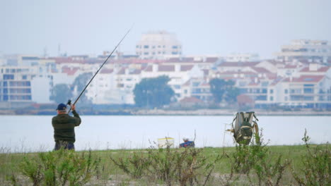 Fisherman-throw-the-line-on-riverside,-urban-buildings-background